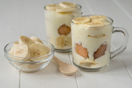 Two glass cups with banana pudding and wooden spoon on a white table. Milk and banana dessert. The concept of dietary vegetarian diet.の写真素材