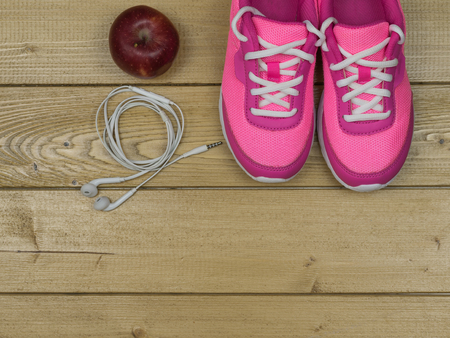 Pink running shoes for fitness classes at the gym and a ripe Apple on a wooden floor. The concept of healthy lifestyle and sports.の写真素材