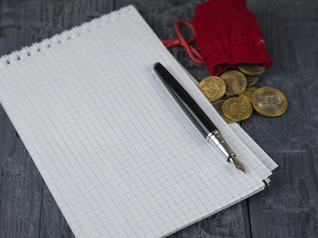Fountain pen, red money bag and notebook on a wooden table. The concept of the accounting of funds.の写真素材