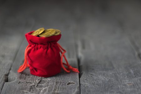 Red velvet pouch with coins on a wooden vintage table. The concept of saving money.の写真素材