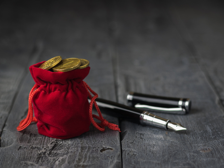 Black fountain pen and a red bag with coins on vintage wooden table. The concept of the accounting of funds.の写真素材