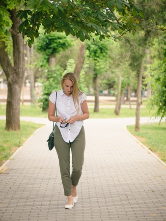 Beautiful woman in a business suit in the alley of the city Park. Portrait of a beautiful woman in full length in the Park.の写真素材