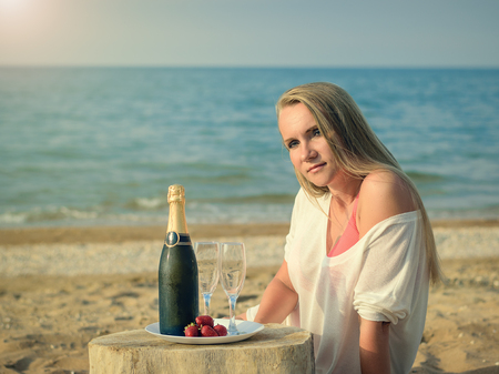 Fresh strawberries on a plate with a bottle of champagne and a beautiful woman by the sea.の写真素材