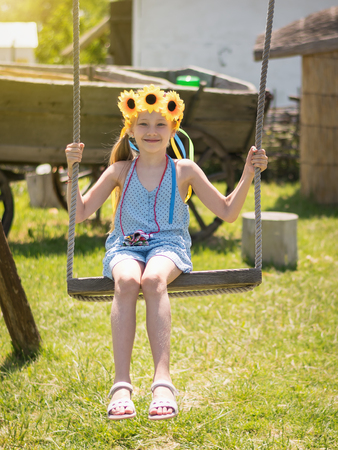 Beautiful girl in the rays of the sun with the decoration of flowers on her head on the old swing. . The attraction of the past.の写真素材