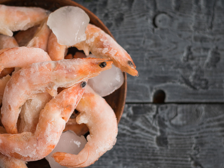 Frozen prawns in an earthenware bowl on a rustic wooden table. Diet seafood.の写真素材