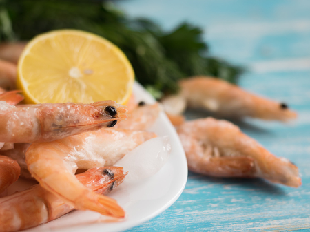 Frozen prawns in an earthenware bowl with lemon and parsley on a wooden table. Diet seafood.の写真素材