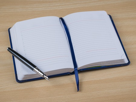 Black fountain pen with note book in blue hardcover in yellow wooden Desk. Place for your text. Top view.の写真素材