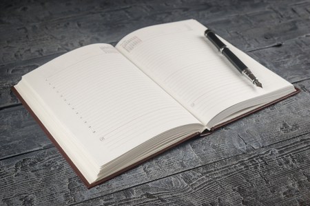 Black fountain pen with note book in blue hardcover in yellow wooden Desk. Place for your text. Top view.の写真素材