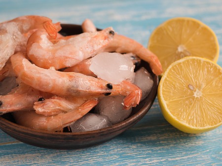 A few frozen shrimp in a clay bowl with lemon on a wooden table.の写真素材