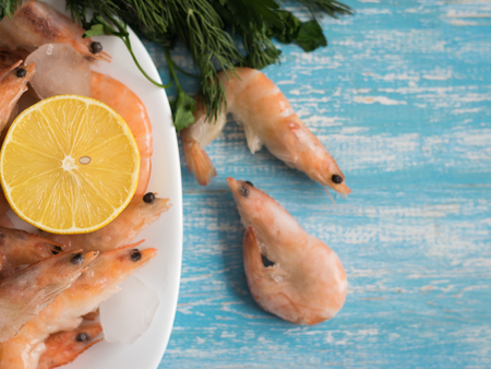 Frozen prawns in an earthenware bowl with lemon and parsley on a wooden table. Diet seafood.の写真素材