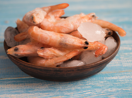 Frozen prawns in an earthenware bowl on a rustic wooden table. Diet seafood.の写真素材