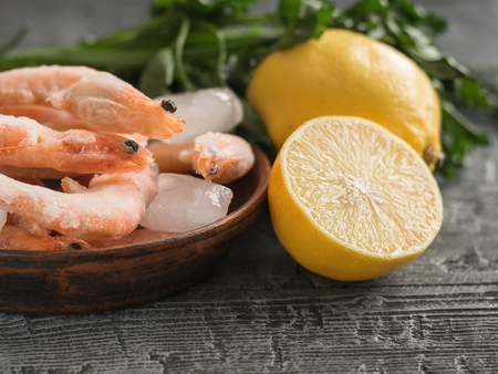 Frozen shrimp with lemon and herbs on cutting Board on wooden table. Diet seafood.の写真素材