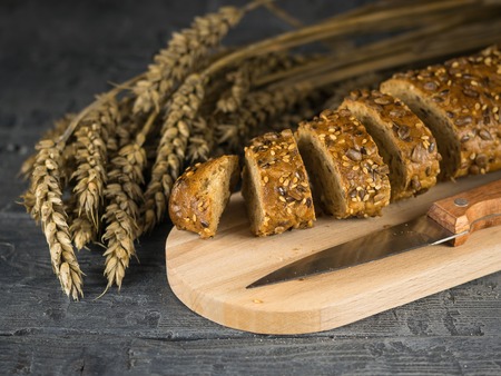 Cut into slices of baguette on a cutting Board and knife on a wooden table. Background of ripe wheat ears.の写真素材