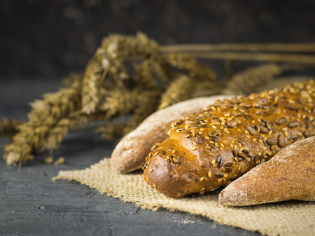 Freshly prepared baguettes on a piece of burlap on a dark table with ears. Background of ripe wheat ears.の写真素材