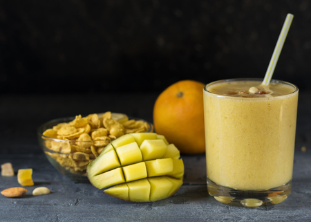 A smoothie of mango, banana, cereal and honey on the dark wooden table in a glass beaker.の写真素材