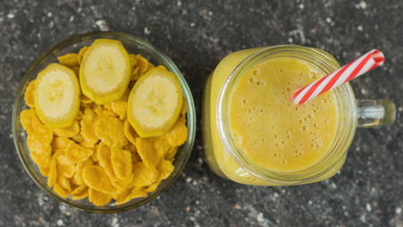 A smoothie of mango, banana, cereal and honey on the dark wooden table in a glass beaker. Diet healthy eating of natural foods. The view from the top.の写真素材