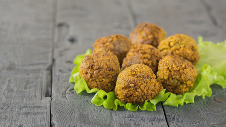 Freshly cooked falafel on lettuce leaves on a dark wooden table with tahini sauce. Eastern vegetarian meal of chickpea.の写真素材