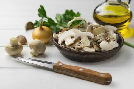Fresh sliced mushrooms in a clay bowl on a white wooden table. Products for vegetarian diet.の写真素材