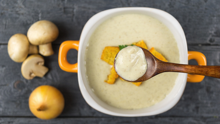 Wooden spoon over a bowl of cream soup from fresh mushrooms. Cream soup of mushrooms, potatoes and cream with spices. The view from the top.の写真素材