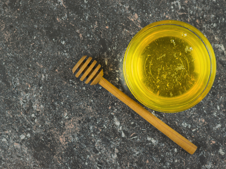 Honey in a glass bowl with a wooden spoon on black stone table. Fresh harvest of honey. The view from the top.の写真素材
