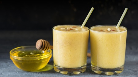 Two glasses of smoothie with banana, mango and cereal on a wooden table with a Cup of honey. Diet healthy eating of natural foods.の写真素材