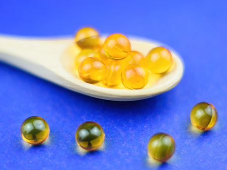 Fish oil capsules in a wooden spoon on a blue background. Selective focus. Traditional medicine.