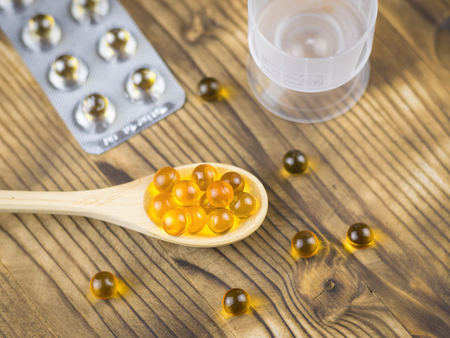 Pills of fish oil a wooden spoon with vials and blister in the background. Treatment natural components. Traditional medicine.の写真素材