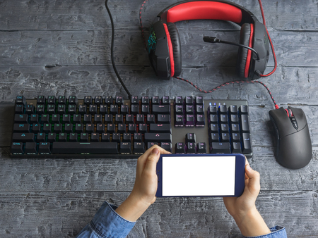Children's hands holding the phone over the Desk with gaming keyboard and mouse. Clipping the background on the device screen.の写真素材