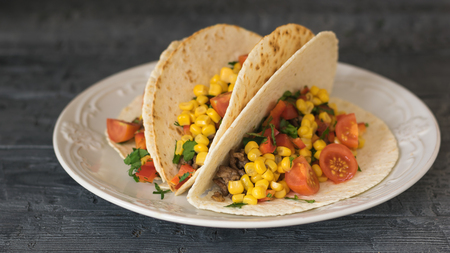 Freshly prepared Mexican tacos on a plate on a rustic table. Tacos, corn, ground beef, pepper, tomato, avocado and herbs.の写真素材