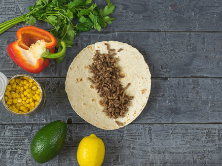 Cake made of cornmeal with ground beef on a wooden table and ingredients for Mexican tacos. A dish of Mexican cuisine. The view from the top.の写真素材
