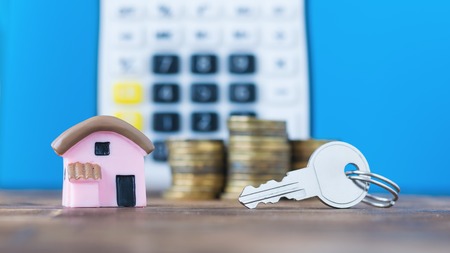 Ceramic model of a house with the coins and key on the background of the calculator. The concept of determining the cost of housing.の写真素材