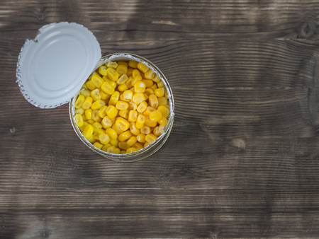 Canned corn in an open aluminum cans on a wooden table. The view from the top. Canned vegetarian food.の写真素材