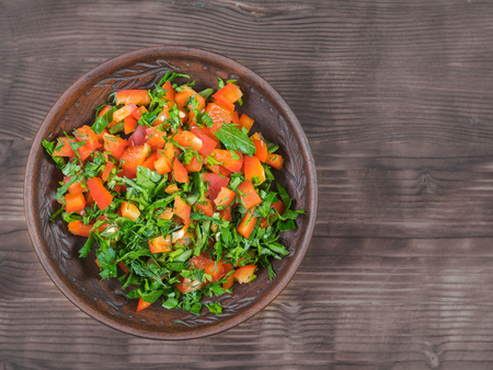 Salad of red bell pepper with herbs in a clay bowl on a wooden table. The view from the top.の写真素材