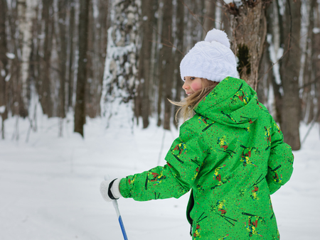 Little girl in a bright green suit learns to ski in the woods. The concept of sports education of children.の写真素材