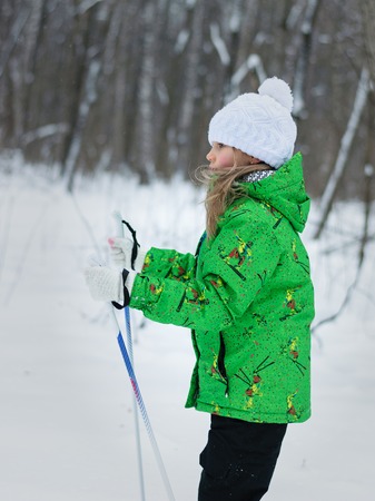 Little girl in a bright green suit learns to ski in the woods. The concept of sports education of children.の写真素材