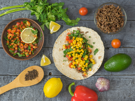 Cake made of cornmeal with ground beef and vegetables Mexican tacos on a wooden table. Ingredients for making Mexican tacos. The view from the top.の写真素材