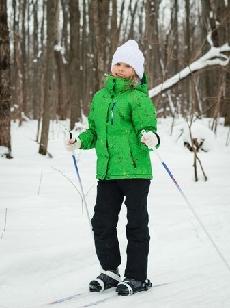 Little girl in a bright green suit learns to ski in the woods. The concept of sports education of children.の写真素材