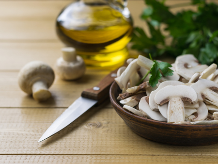 Fresh sliced mushrooms in a clay bowl and parsley on a wooden table. Products for vegetarian diet.の写真素材