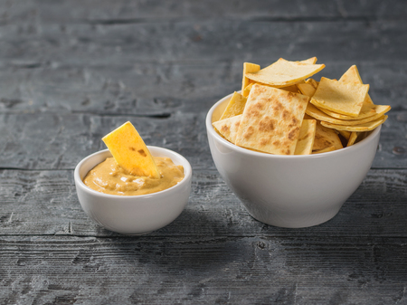 Mexican tortilla chips with cheese and mustard in a clay bowl on a black wooden table. A dish of Mexican cuisine.の写真素材