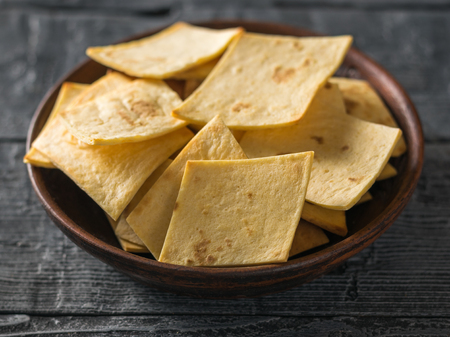 Mexican tortilla chips with cheese in a clay bowl on a black wooden table. A dish of Mexican cuisine.の写真素材
