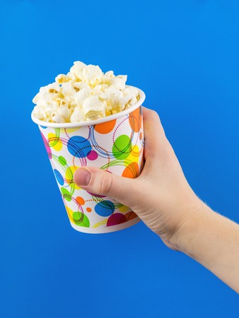 The child holds a multicolored glass of popcorn on a blue background.の写真素材