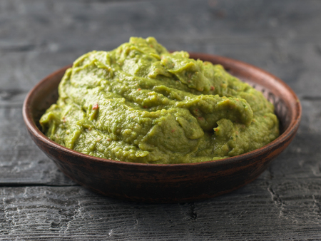 Freshly made guacamole in a clay bowl on a dark rustic table. Raw food.の写真素材