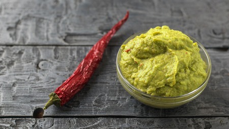 Freshly made guacamole in a bowl and chili pepper on a dark rustic table.の写真素材
