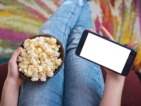 Girl holding a phone with clipping background. A bowl of popcorn on the childs lap.の写真素材
