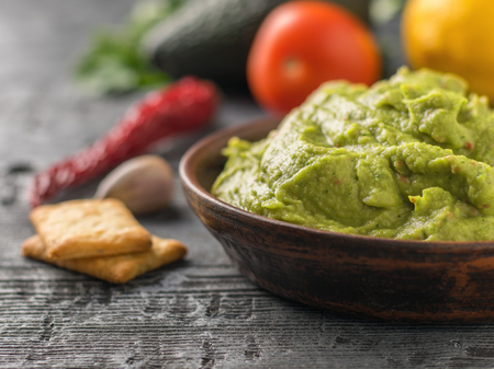Clay bowl with fresh guacamole, tomatoes, lemon, chips and garlic on wooden table. Diet vegetarian Mexican food avocado.の写真素材