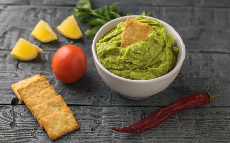 White bowl with fresh guacamole, tomatoes, lemon, chips and garlic on wooden table. Diet vegetarian Mexican food avocado. Raw food.の写真素材