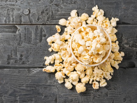 Popcorn is poured from a multi-colored paper Cup on a rustic table. Vegetarian food from corn.の写真素材