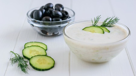 Freshly made tzatziki in a glass bowl with olives on a white wooden table. Vegetarian Greek cuisine.の写真素材