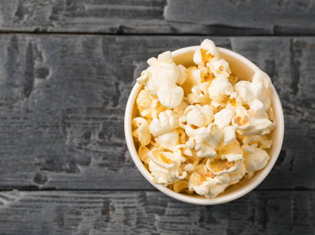 Popcorn is poured from a multi-colored paper Cup on a rustic table. Vegetarian food from corn.の写真素材