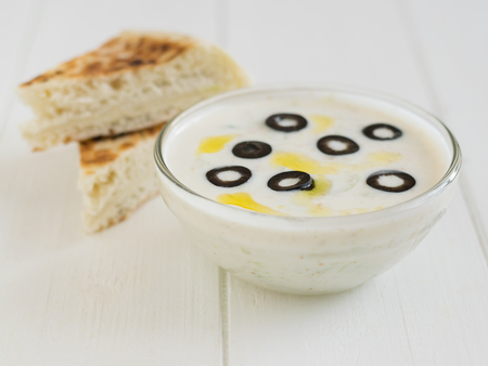 Freshly made tzatziki in a glass bowl with olives on a white wooden table. Vegetarian Greek cuisine.の写真素材